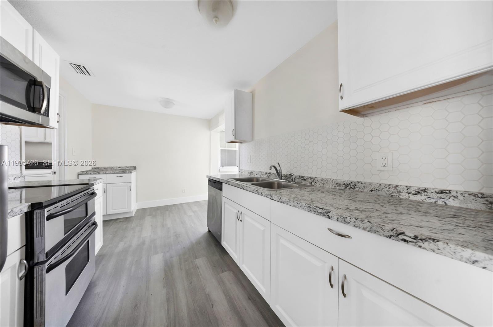 A kitchen features white cabinets, granite countertops, a hexagonal tile backsplash, and gray flooring — 2520 NW 2nd Dr, Pompano Beach FL 33064, POMPANO BEACH, FL