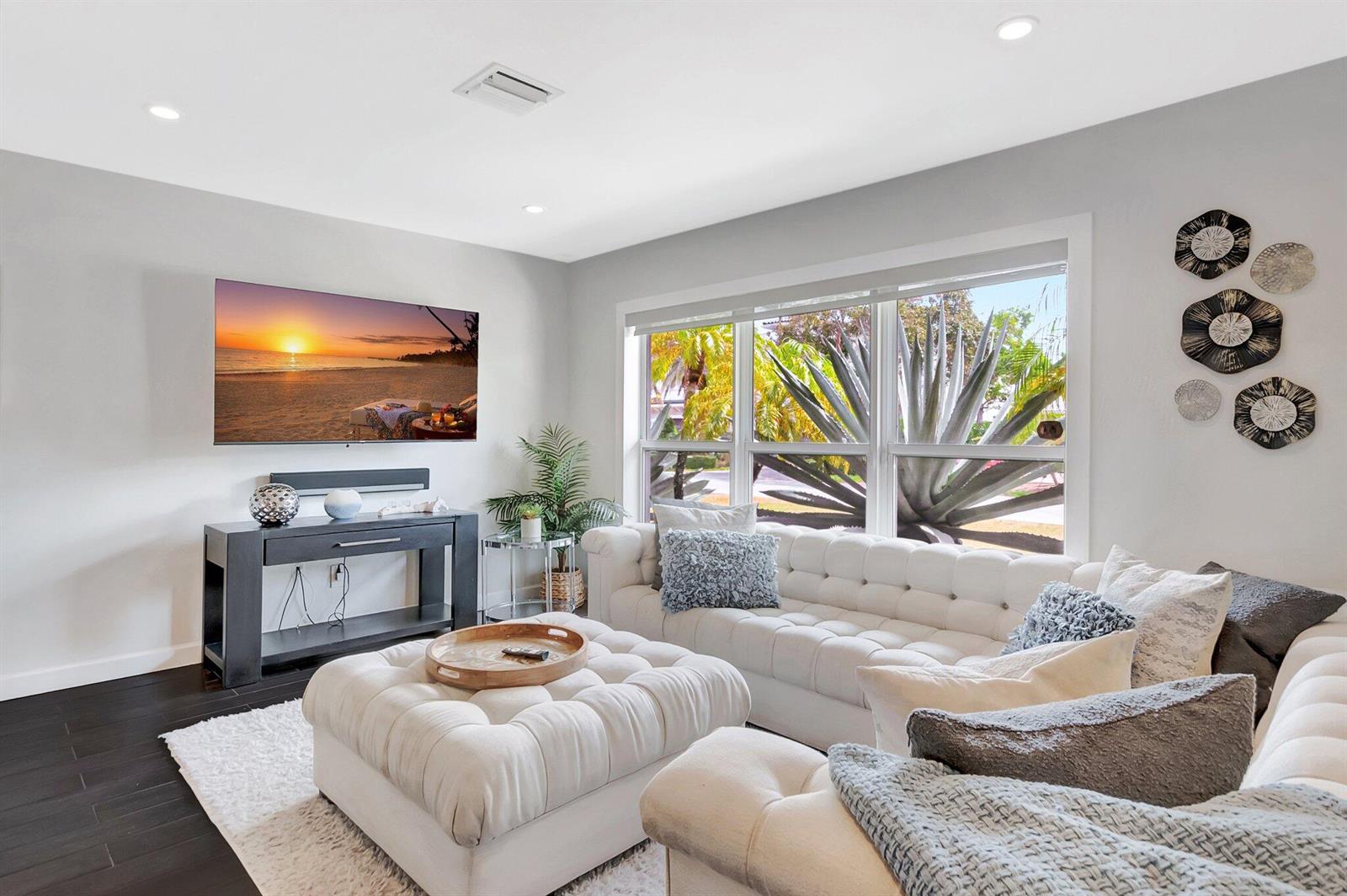A living room features a white tufted sofa, matching ottoman, dark flooring, and a wall-mounted television — 855 Berkeley Street, Boca Raton FL 33487, BOCA RATON, FL