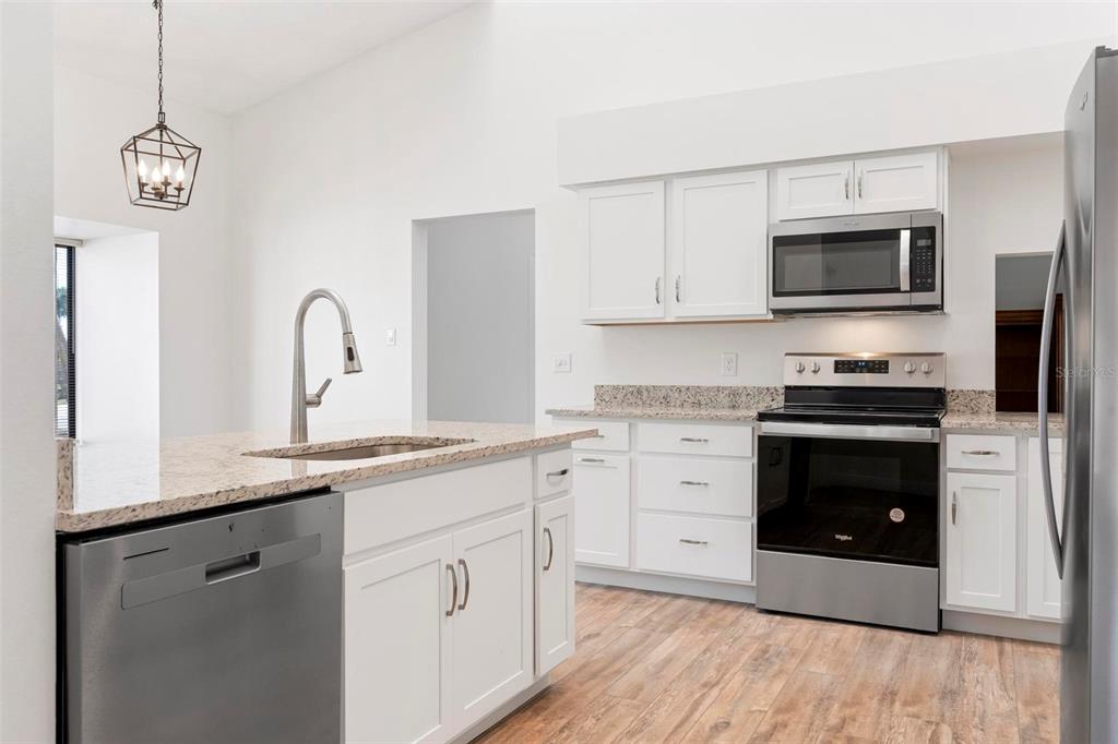 A kitchen features white cabinets, granite countertops, stainless steel appliances, and wood-look flooring — 3 INLETS BOULEVARD UNIT 3, NOKOMIS, FL