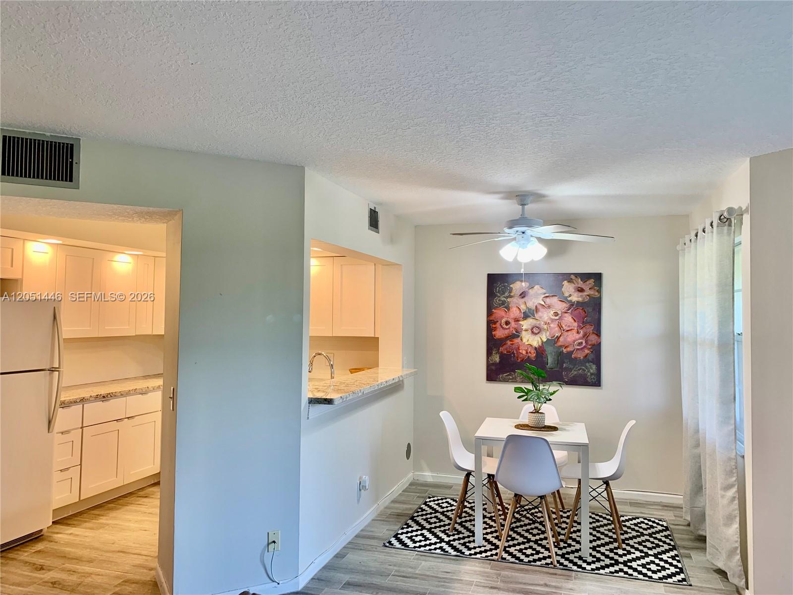 A dining area with a white table and chairs sits beside a kitchen pass-through window — PEMBROKE PINES, FL