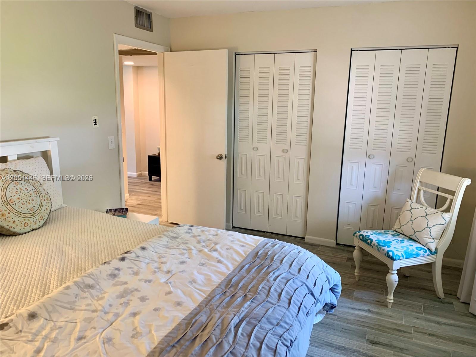 A bedroom features a bed, a white chair, and two sets of louvered closet doors — PEMBROKE PINES, FL