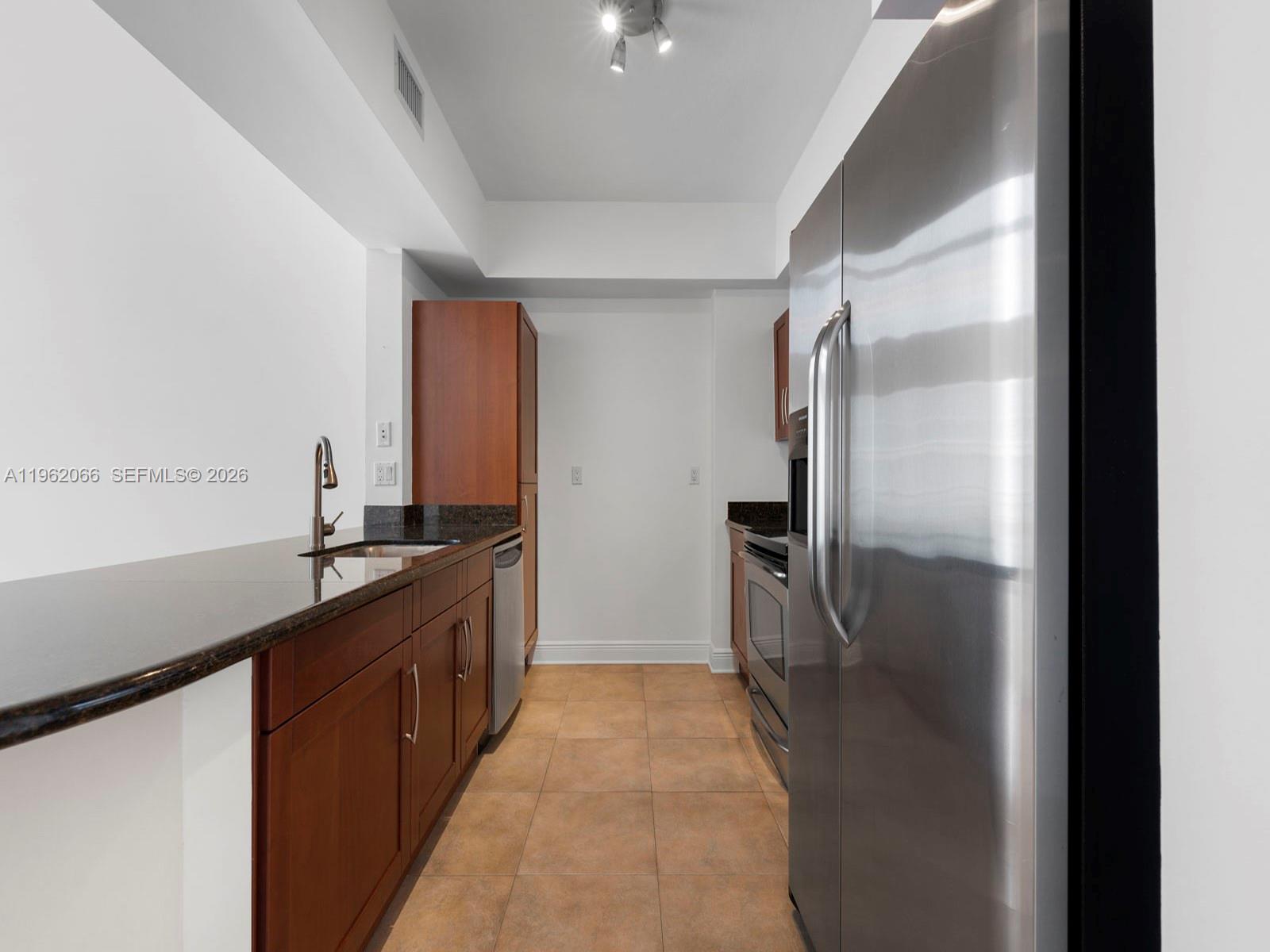 A galley kitchen features wood cabinets, dark granite countertops, and stainless steel appliances — 7265 SW 89th St # A520, Miami FL 33156, MIAMI, FL
