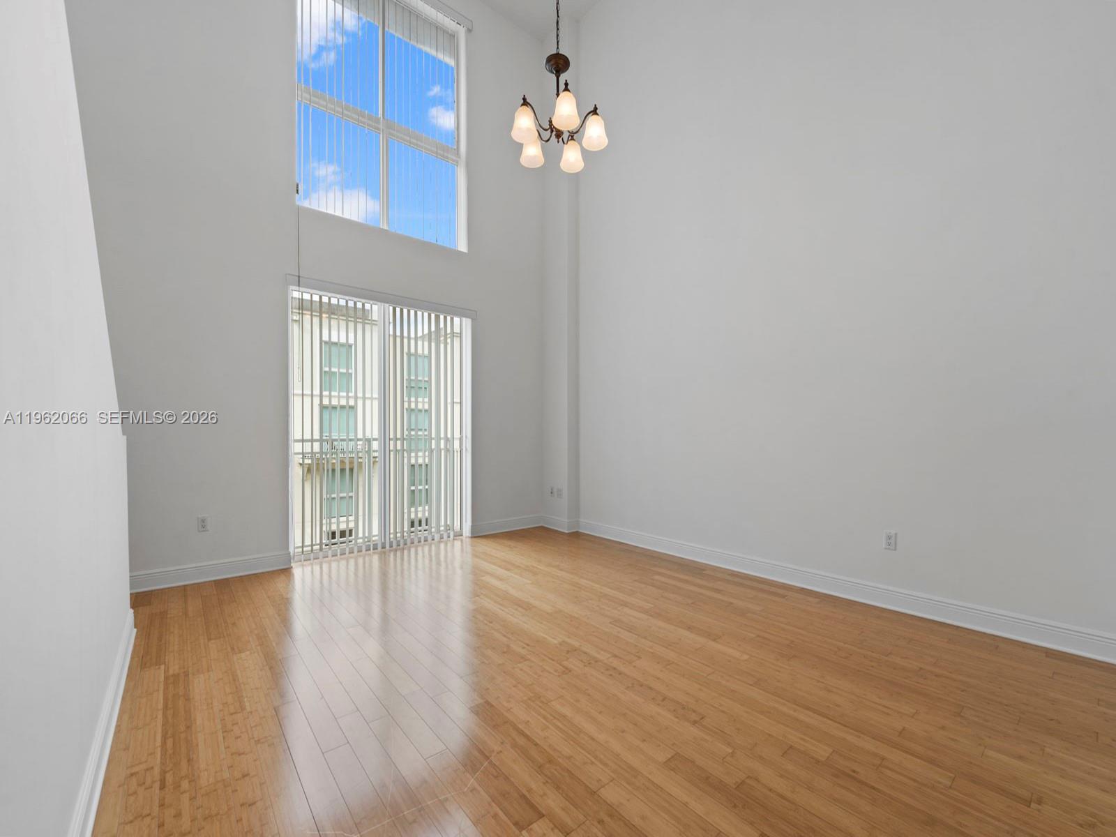 A bright, empty room features high ceilings, light wood flooring, a chandelier, and large windows — 7265 SW 89th St # A520, Miami FL 33156, MIAMI, FL