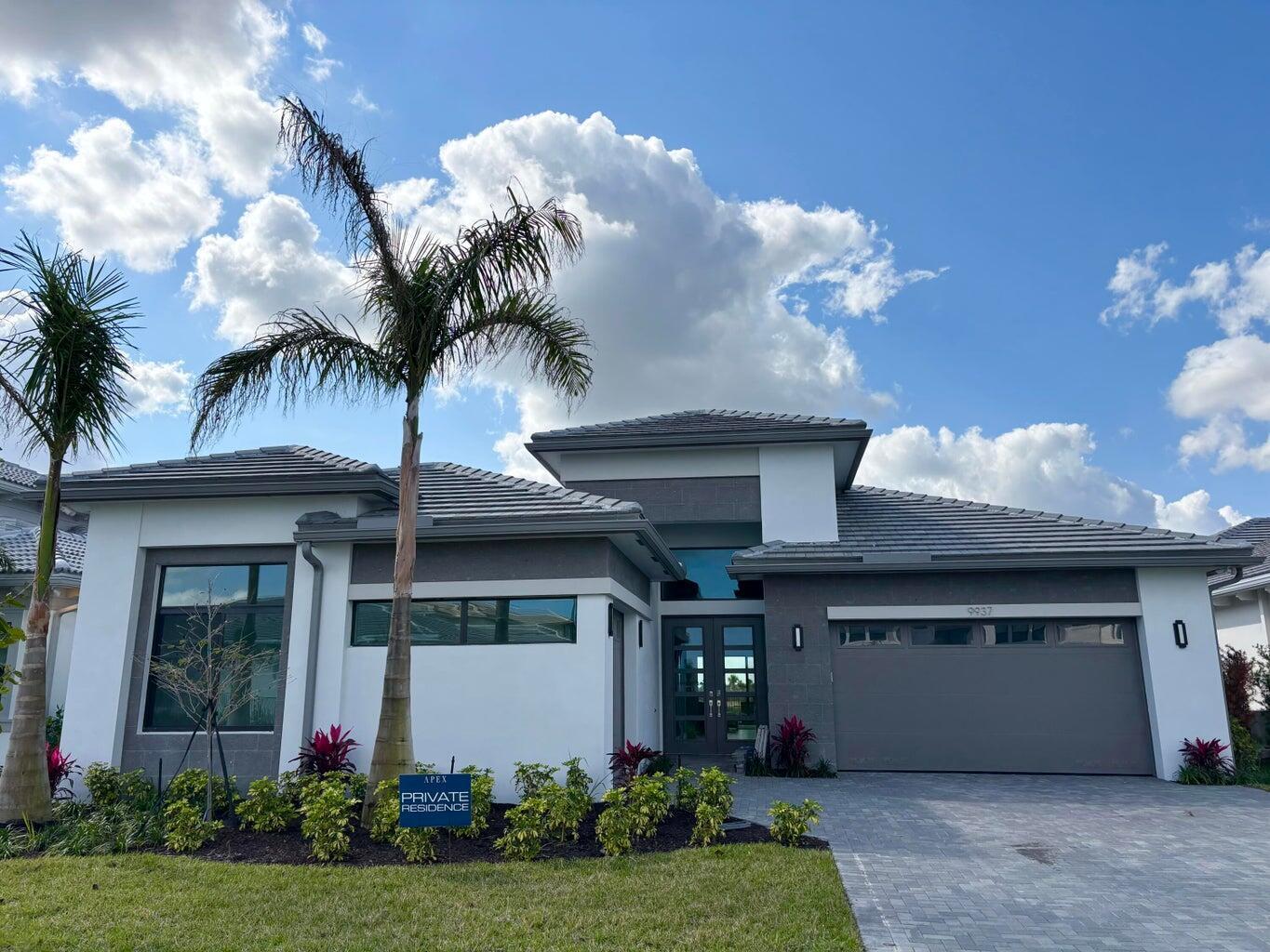 A modern single-story house with a gray tile roof, white stucco walls, and a paved driveway — 9937 Migration Point, Palm Beach Gardens FL 33412, PALM BEACH GARDENS, FL