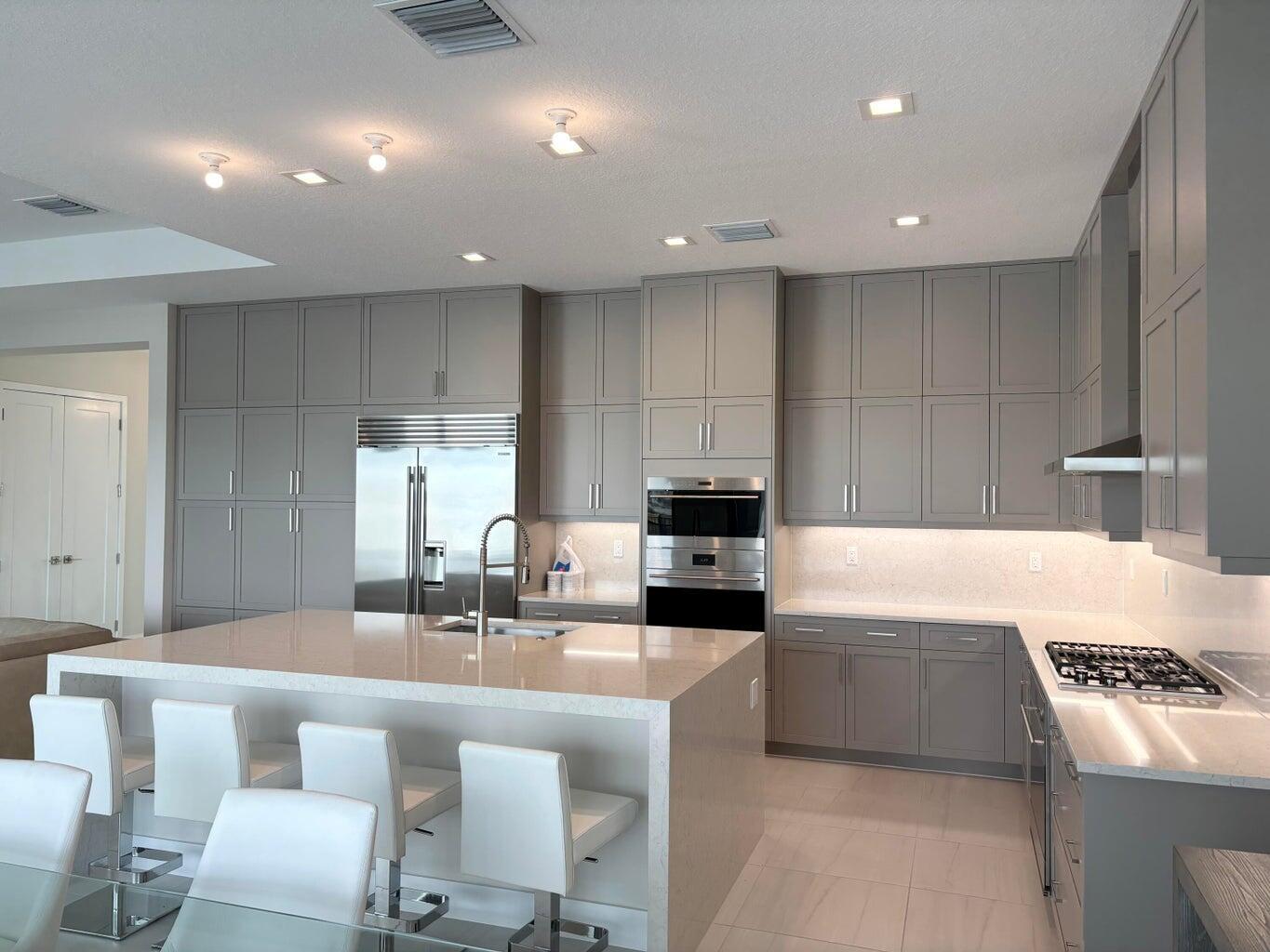 A modern kitchen features gray shaker cabinets, a large quartz island, and stainless steel appliances — 9937 Migration Point, Palm Beach Gardens FL 33412, PALM BEACH GARDENS, FL