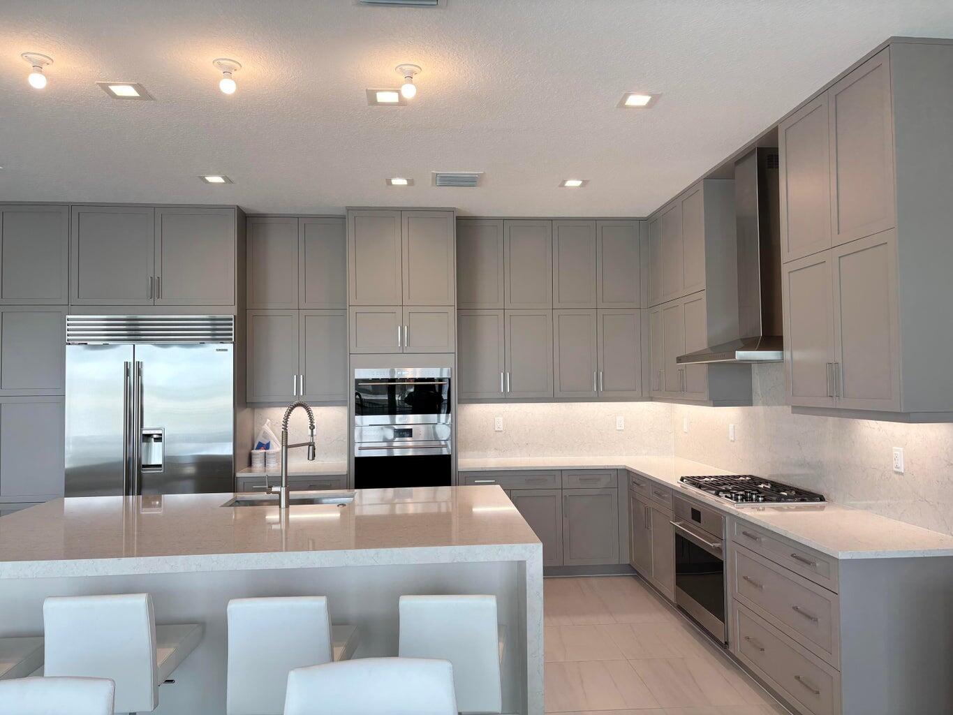 A modern kitchen features gray shaker cabinets, stainless steel appliances, and a large quartz island — 9937 Migration Point, Palm Beach Gardens FL 33412, PALM BEACH GARDENS, FL