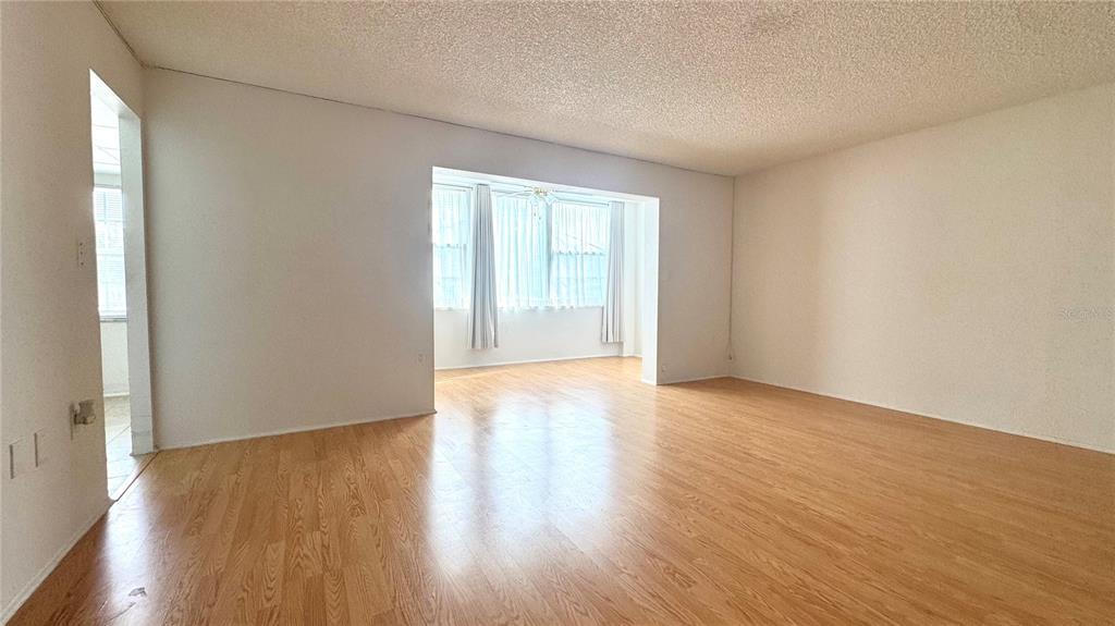 An empty living room features light wood-look flooring, white walls, and a large windowed alcove — 1900 68TH STREET N UNIT 106, ST PETERSBURG, FL