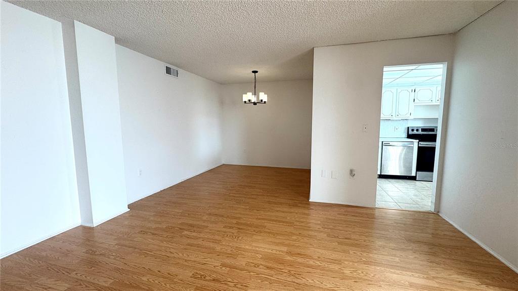 An empty room with light wood-look flooring leads to a kitchen through a doorway — 1900 68TH STREET N UNIT 106, ST PETERSBURG, FL