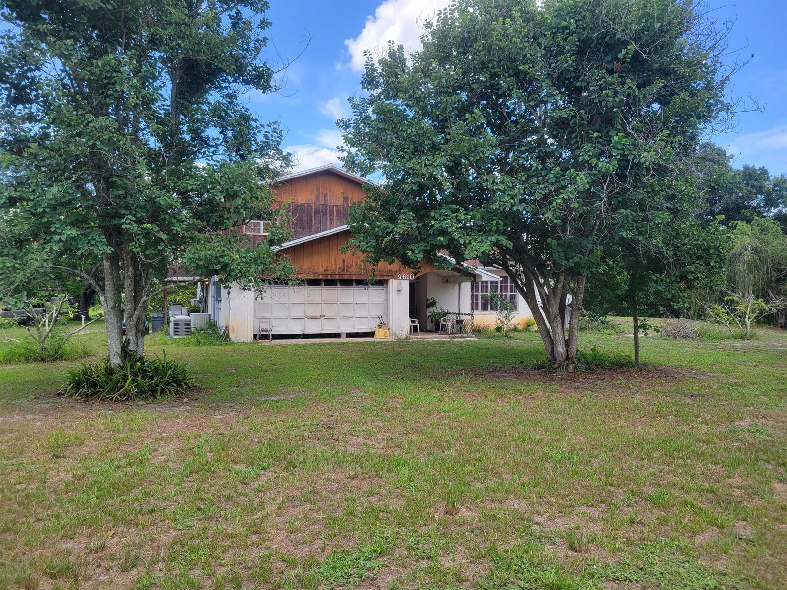 A two-story house with wood siding and a white garage sits on a grassy lot — 9610 Orange Avenue, Fort Pierce FL 34945, FORT PIERCE, FL