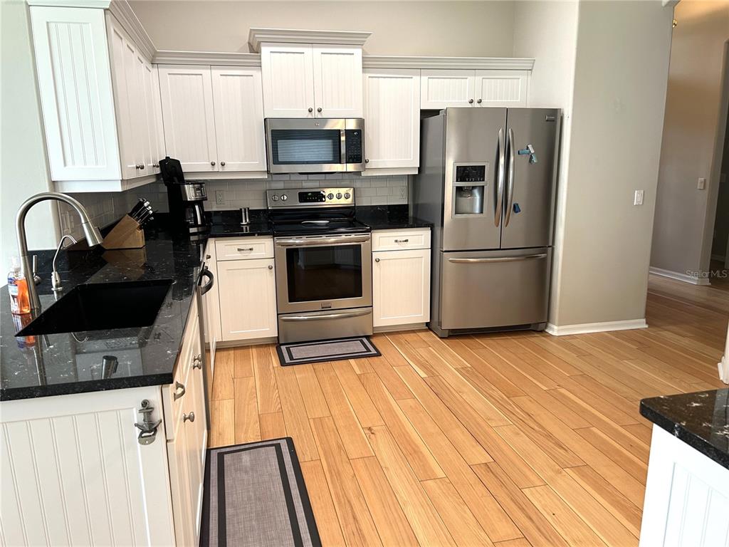 A kitchen features white cabinets, stainless steel appliances, black countertops, and light wood flooring — 8918 OLDE HICKORY AVENUE, SARASOTA, FL