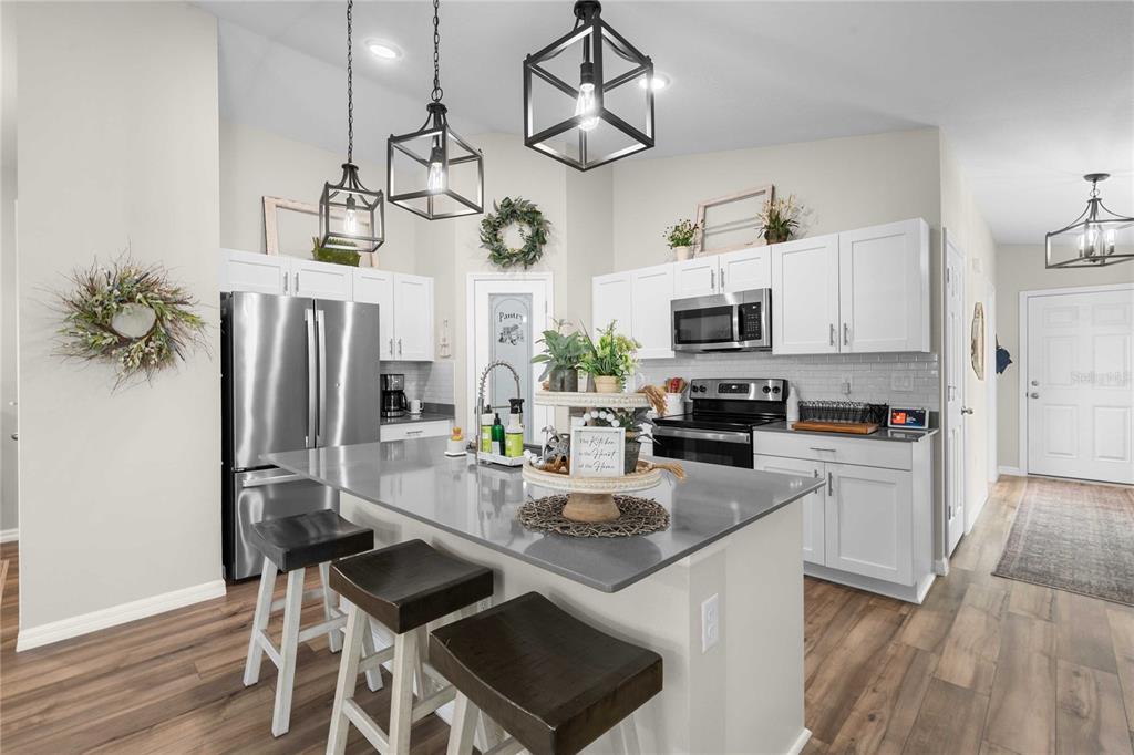 A modern kitchen features white cabinetry, stainless steel appliances, a gray island, and pendant lighting — 34102 SCARLET SAGE COURT, WESLEY CHAPEL, FL