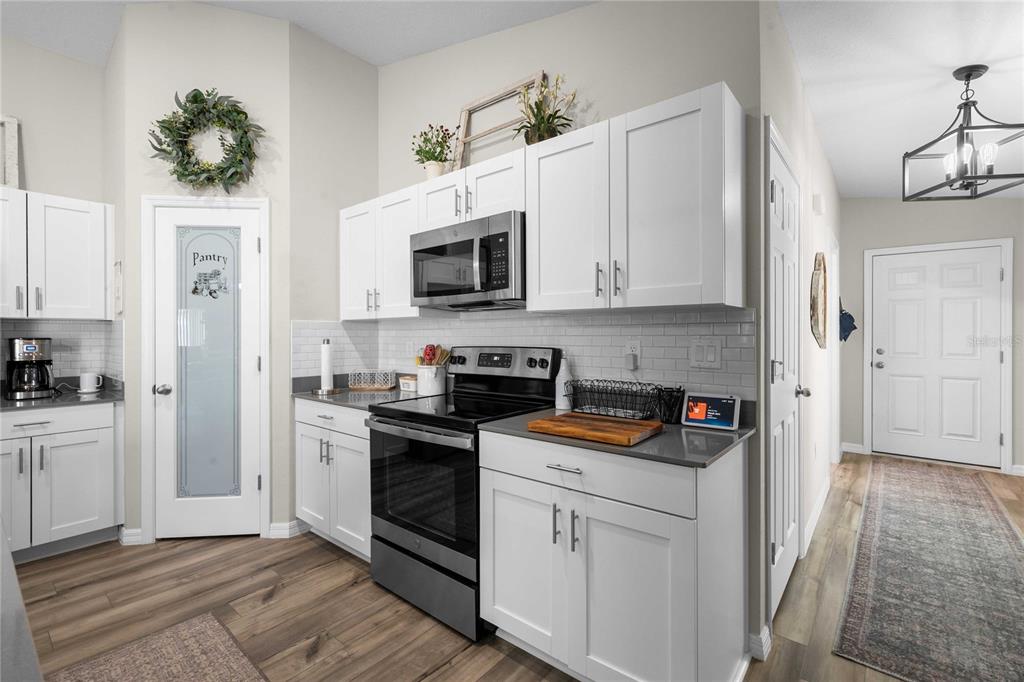 A kitchen features white cabinets, gray countertops, a subway tile backsplash, and stainless steel appliances — 34102 SCARLET SAGE COURT, WESLEY CHAPEL, FL