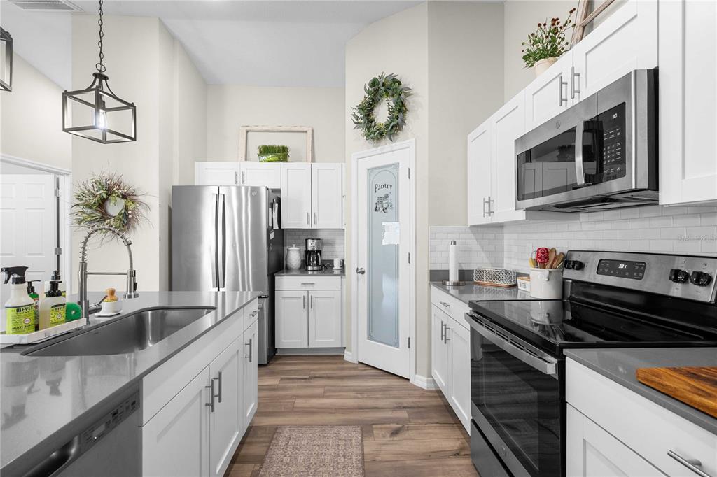 A modern kitchen features white cabinets, stainless steel appliances, a center island, and wood flooring — 34102 SCARLET SAGE COURT, WESLEY CHAPEL, FL