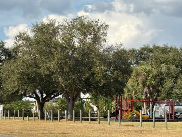 A playground with a slide and climbing structure sits beneath large trees in a park — JOSLYN TERRACE, PORT CHARLOTTE, FL
