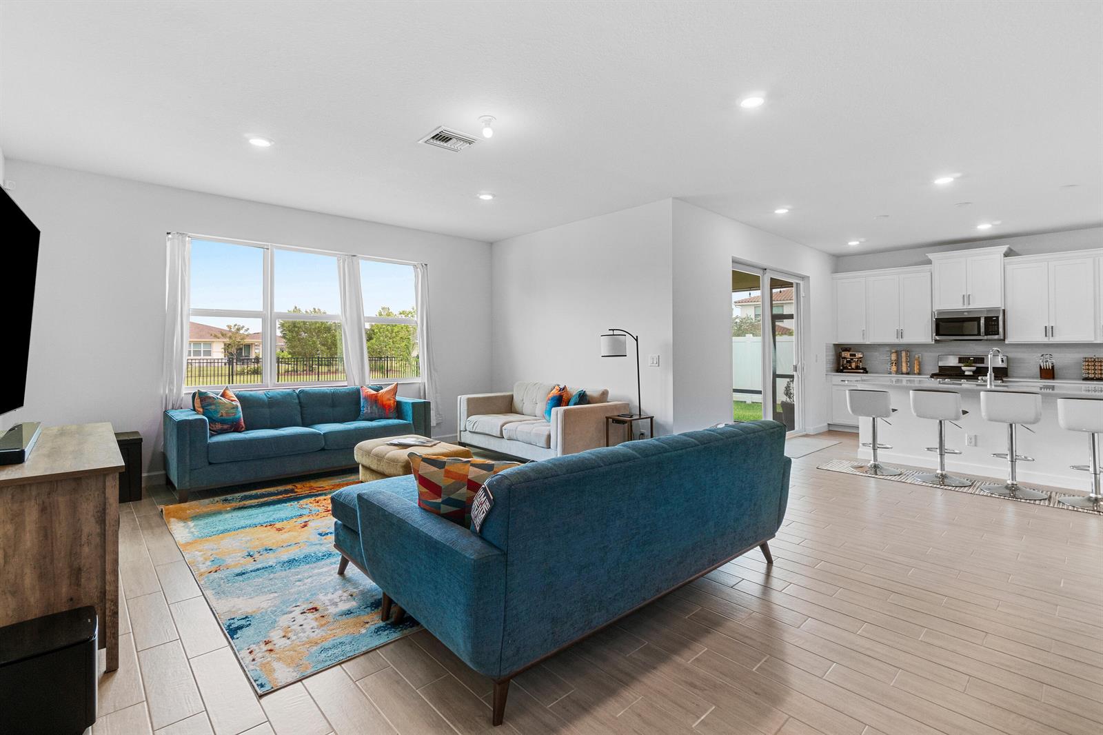 A living room with blue sofas and a colorful rug opens to a white kitchen — 1218 Timber Reap Trail, FL 33470, FL