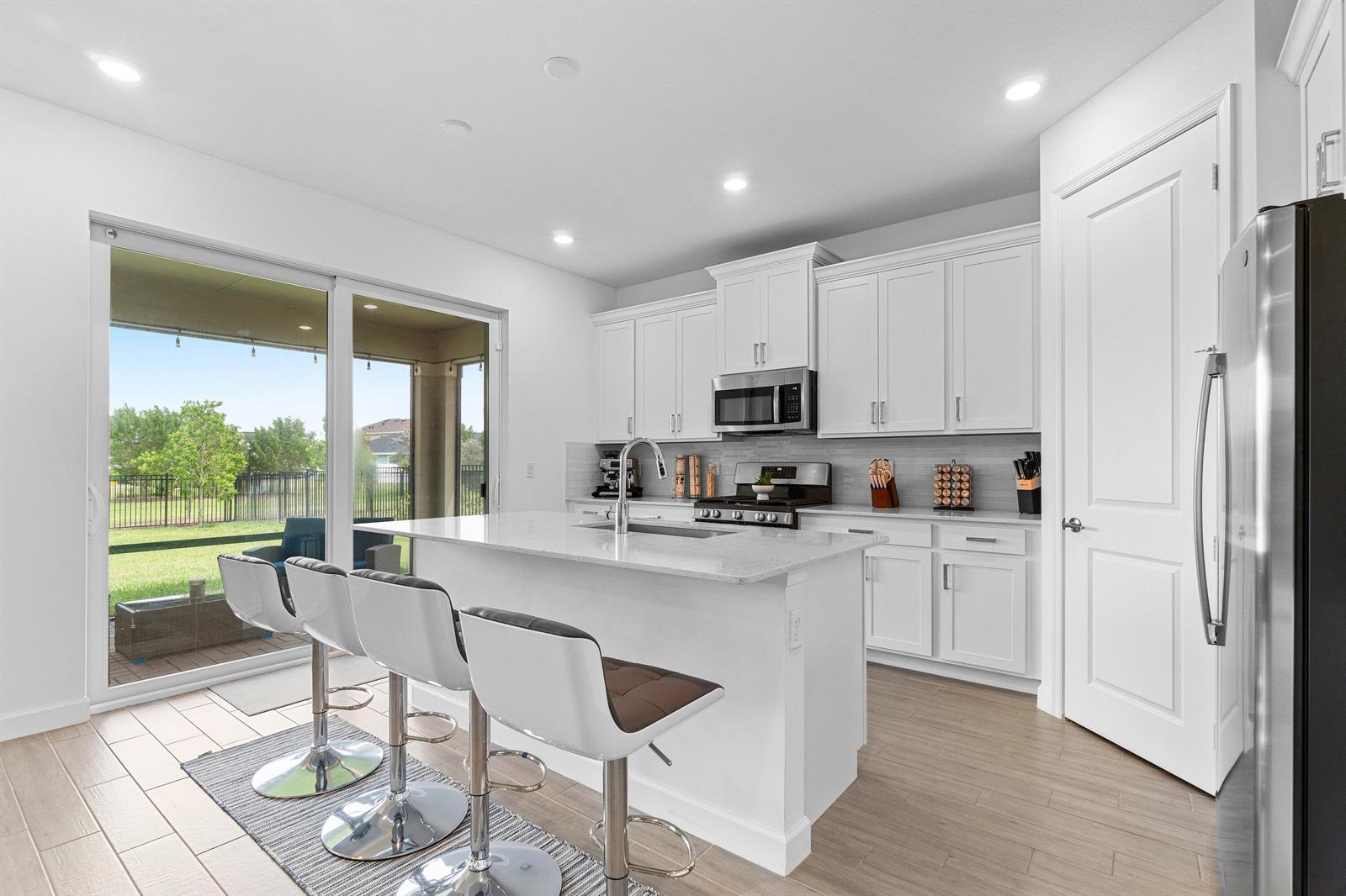 A modern kitchen features white cabinets, a central island with bar stools, and sliding doors — 1218 Timber Reap Trail, FL 33470, FL