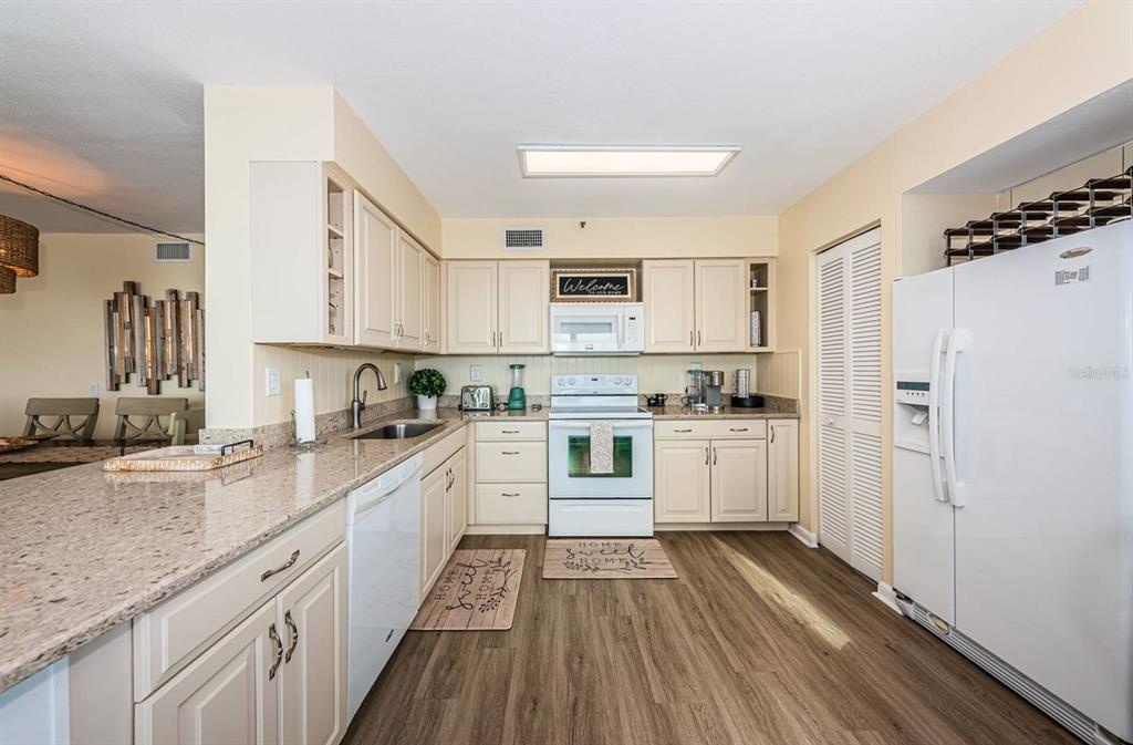 A kitchen features light-colored cabinets, granite countertops, white appliances, and wood-look flooring — 6291 BAHIA DEL MAR CIRCLE UNIT 903, ST PETERSBURG, FL