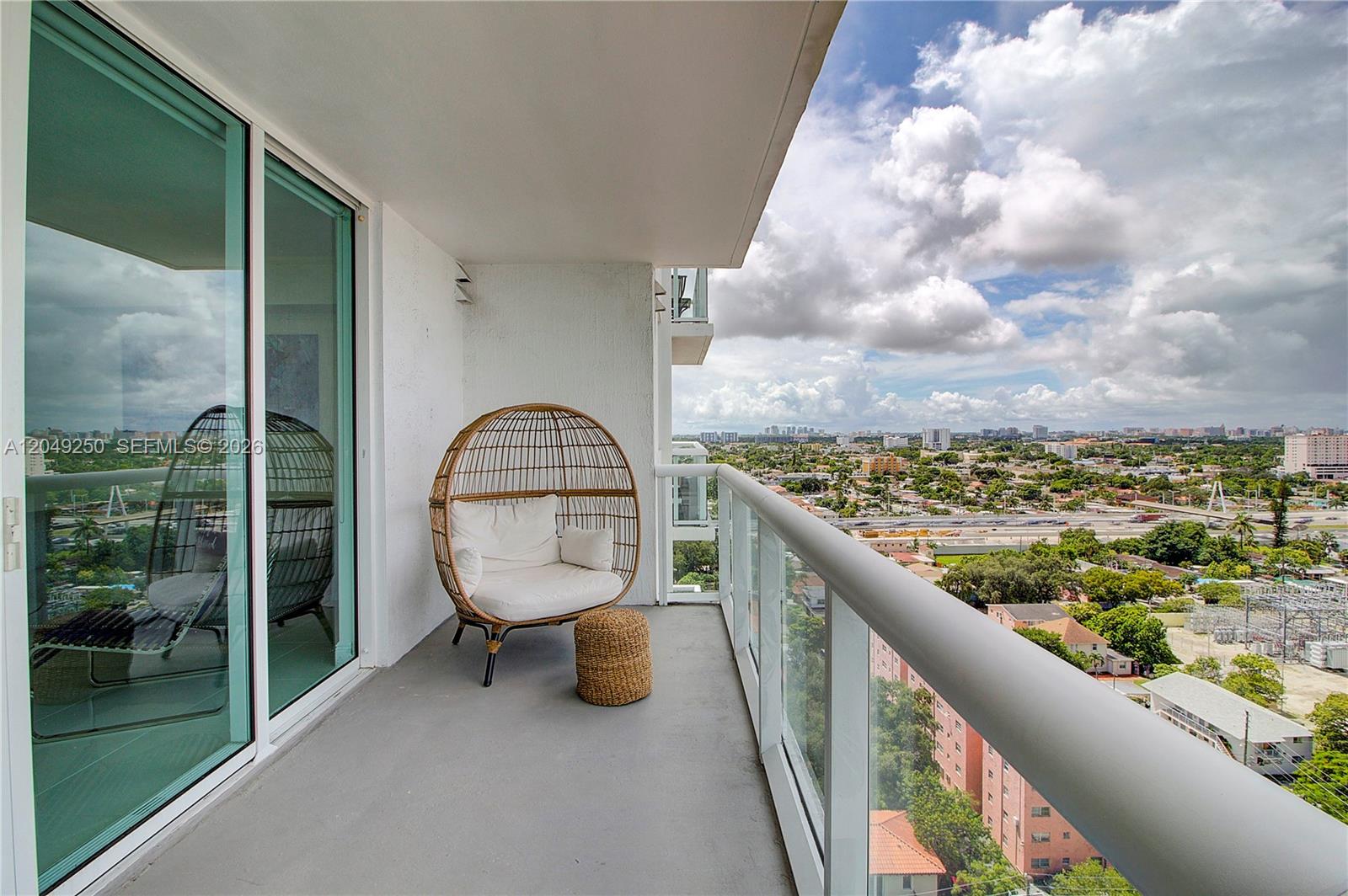 A balcony with a wicker egg chair overlooks a city landscape under a cloudy sky — 1871 NW S River Dr # 1804, Miami FL 33125, MIAMI, FL