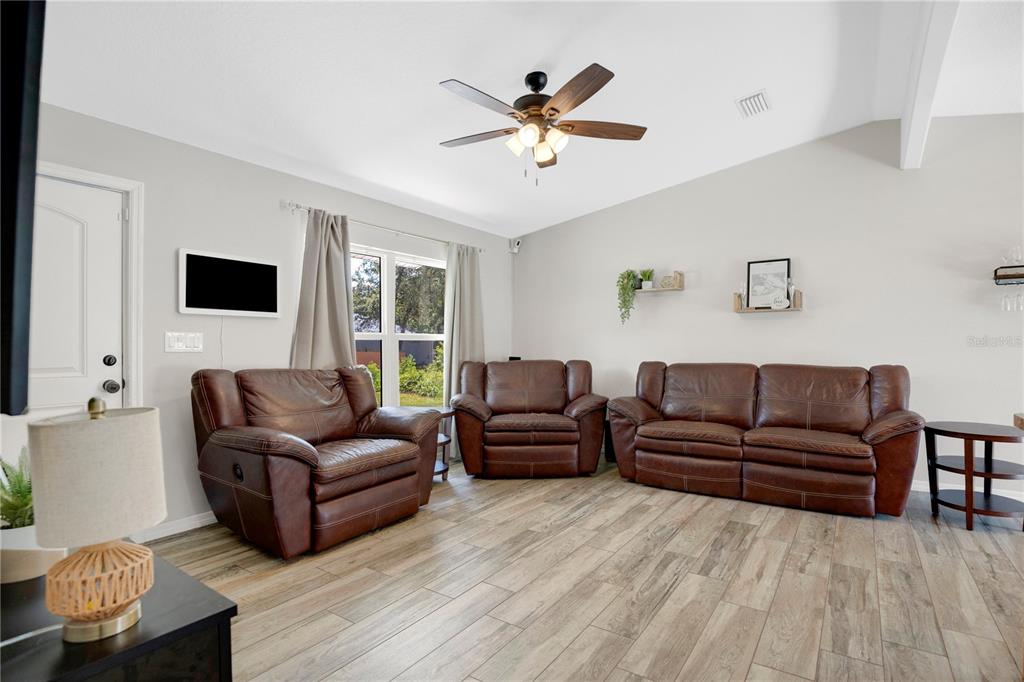 A living room features brown leather furniture, wood-look tile flooring, and a ceiling fan — 1345 GRAND AVENUE, ORANGE CITY, FL