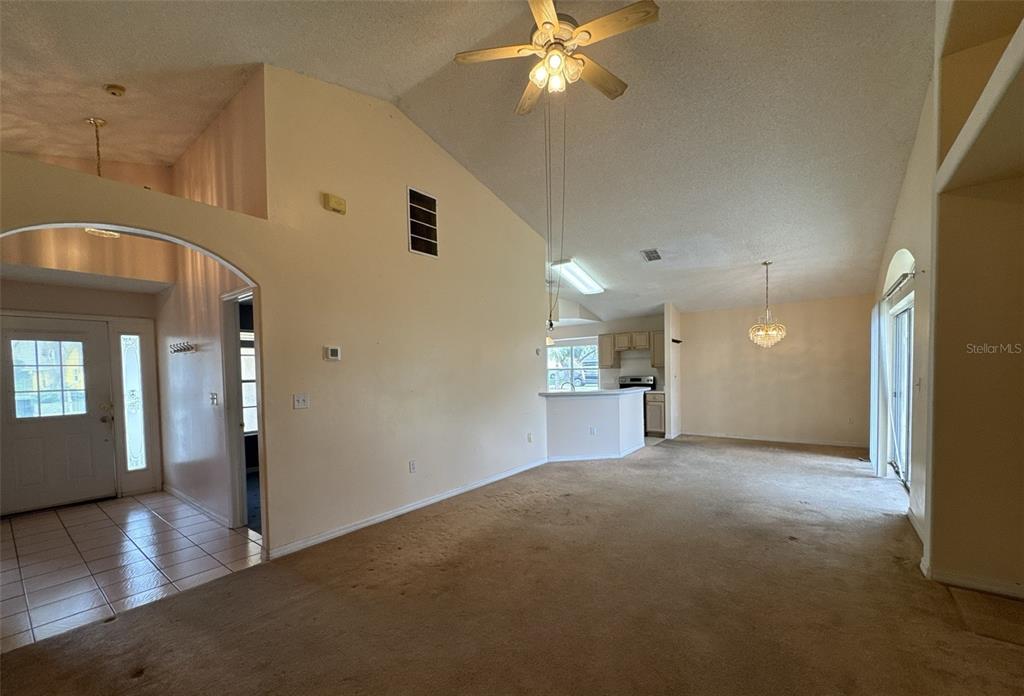 A living room with beige carpet, vaulted ceilings, a ceiling fan, and an adjacent kitchen — 357 THORNBUSH PARKWAY, DAVENPORT, FL