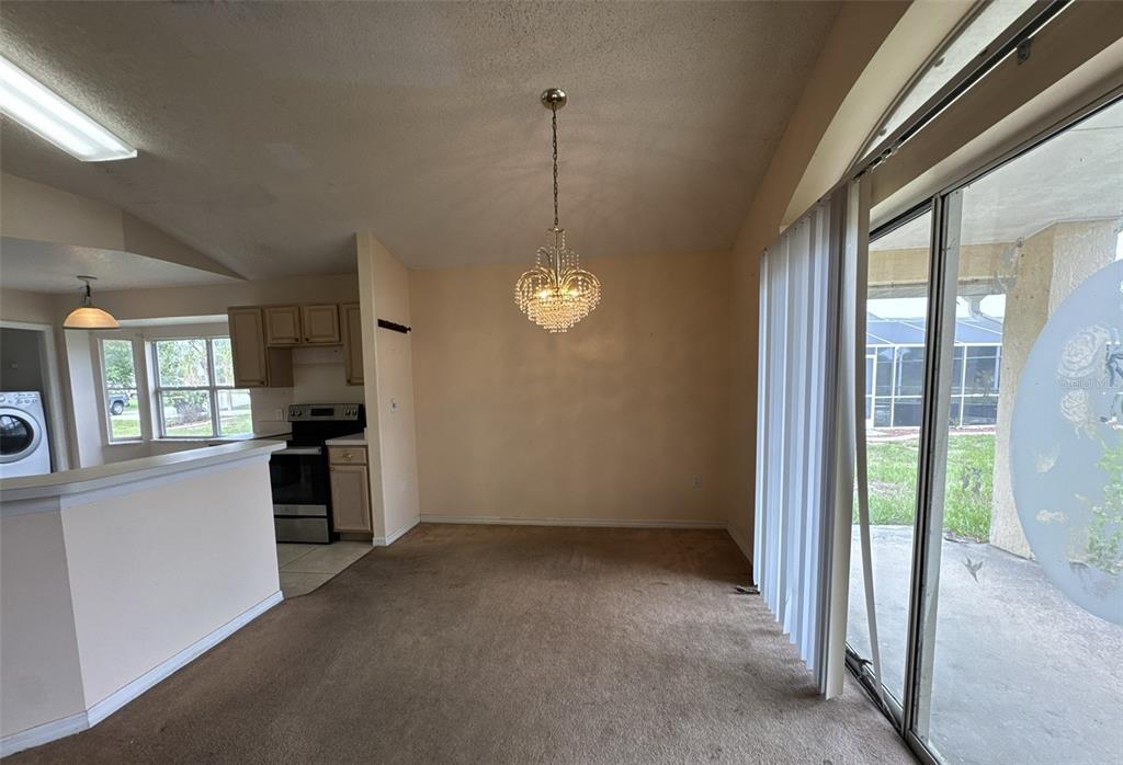 A dining area with brown carpet, a crystal chandelier, and a sliding glass door — 357 THORNBUSH PARKWAY, DAVENPORT, FL