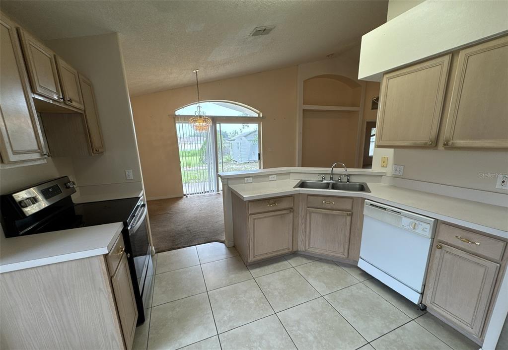 A kitchen with light wood cabinets, white countertops, and tile flooring overlooks a carpeted living area — 357 THORNBUSH PARKWAY, DAVENPORT, FL
