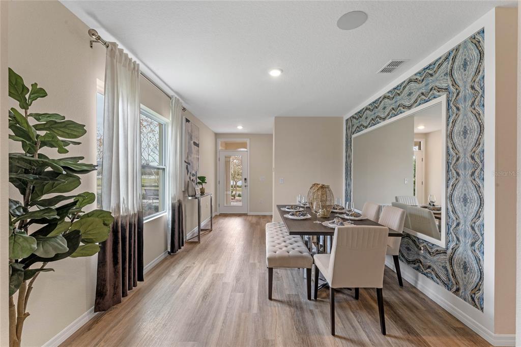 A dining room features a large mirror, patterned wallpaper, a table with chairs, and wood-look flooring — 3011 GREY MOSS DRIVE, ST CLOUD, FL