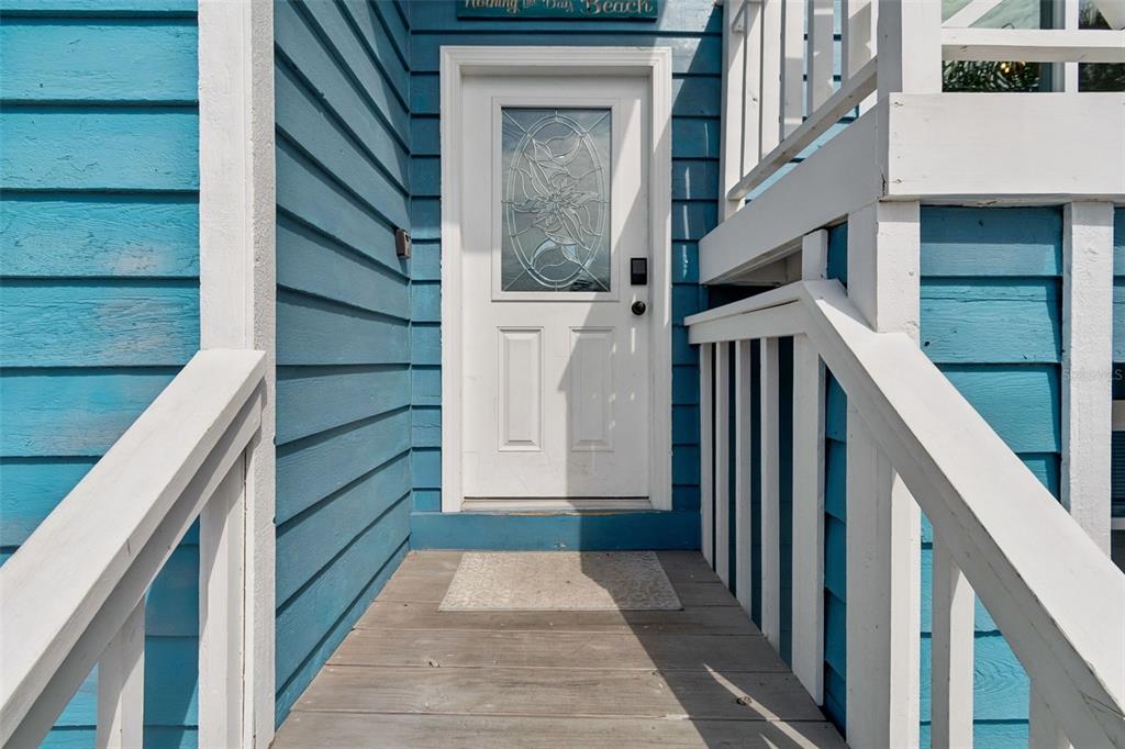 A white front door with a decorative glass window sits on a wooden porch — 330 6TH AVENUE, INDIAN ROCKS BEACH, FL
