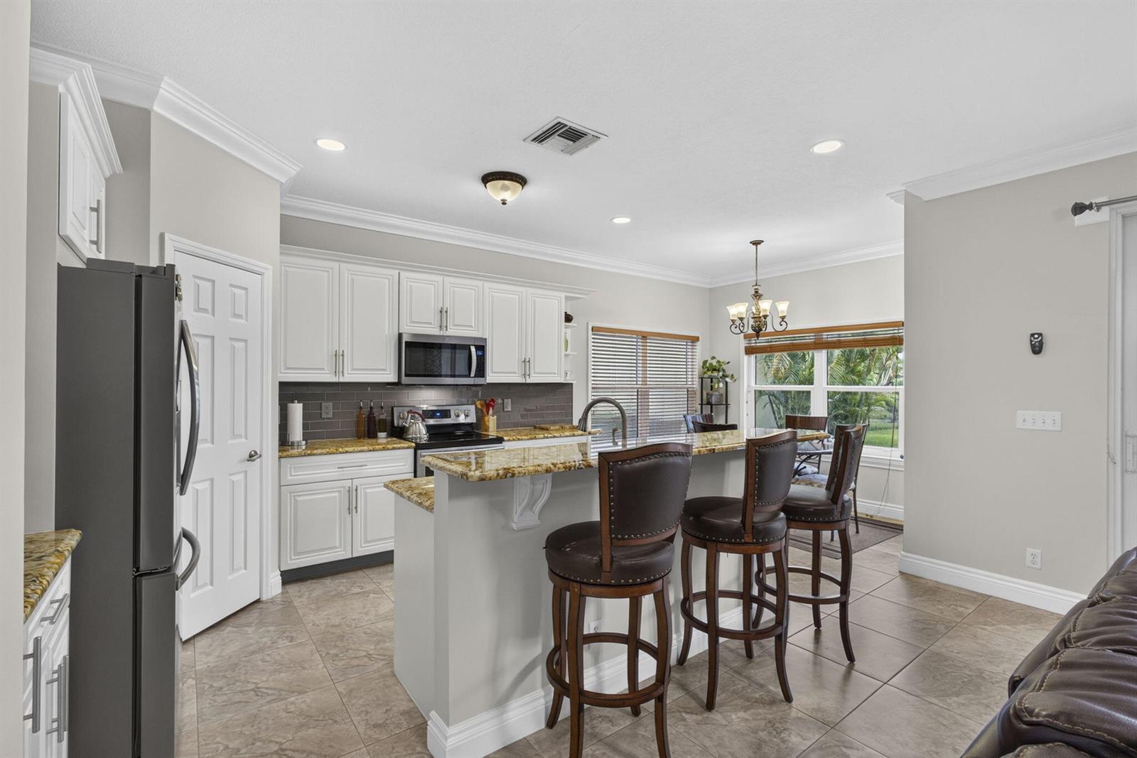 A kitchen features white cabinets, granite countertops, a breakfast bar with stools, and tile flooring — 11483 Beacon Pointe Lane, Wellington FL 33414, WELLINGTON, FL