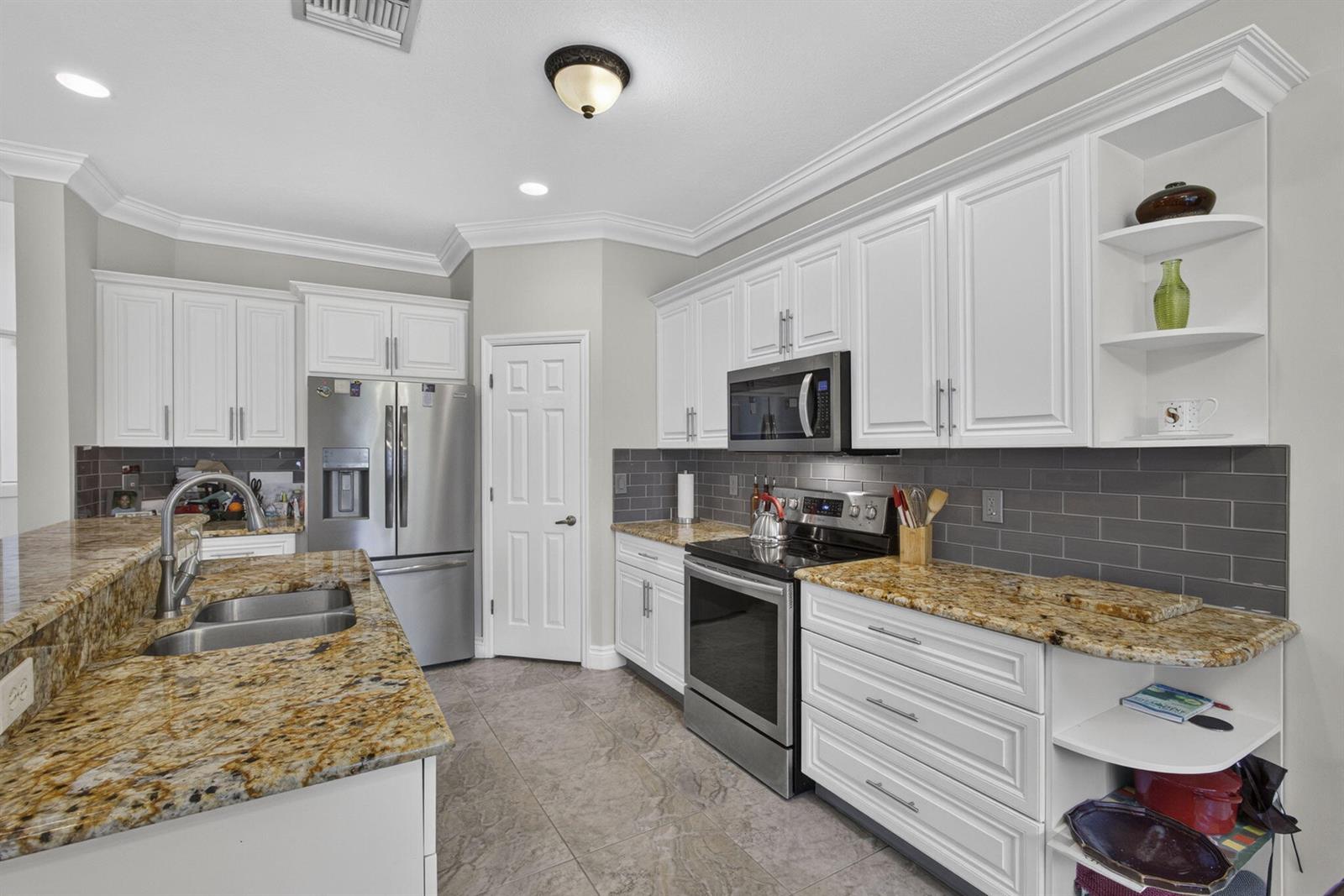 A kitchen features white cabinetry, granite countertops, stainless steel appliances, and a gray subway tile backsplash — 11483 Beacon Pointe Lane, Wellington FL 33414, WELLINGTON, FL
