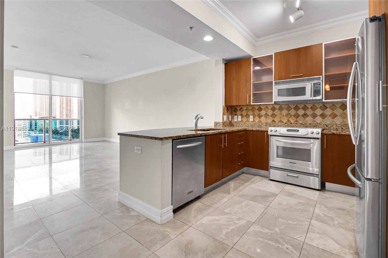 A kitchen with wood cabinets, stainless steel appliances, and tile flooring opens to a living area — 1945 S Ocean Dr # 1410, Hallandale Beach FL 33009, HALLANDALE BEACH, FL