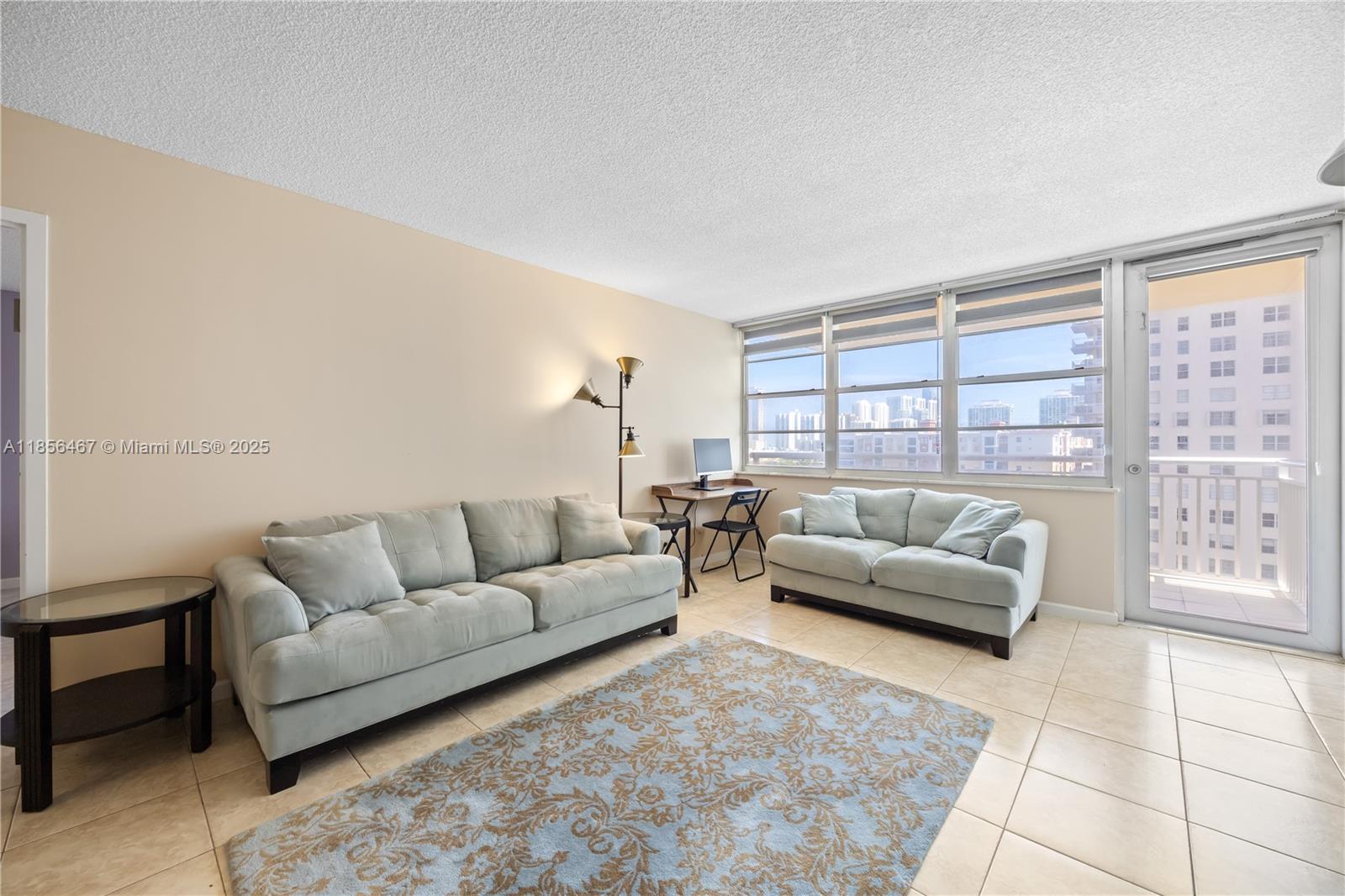 A living room features light-colored sofas, a desk, tile flooring, and a balcony with city views — 251 174th St # 812, Sunny Isles Beach FL 33160, SUNNY ISLES BEACH, FL