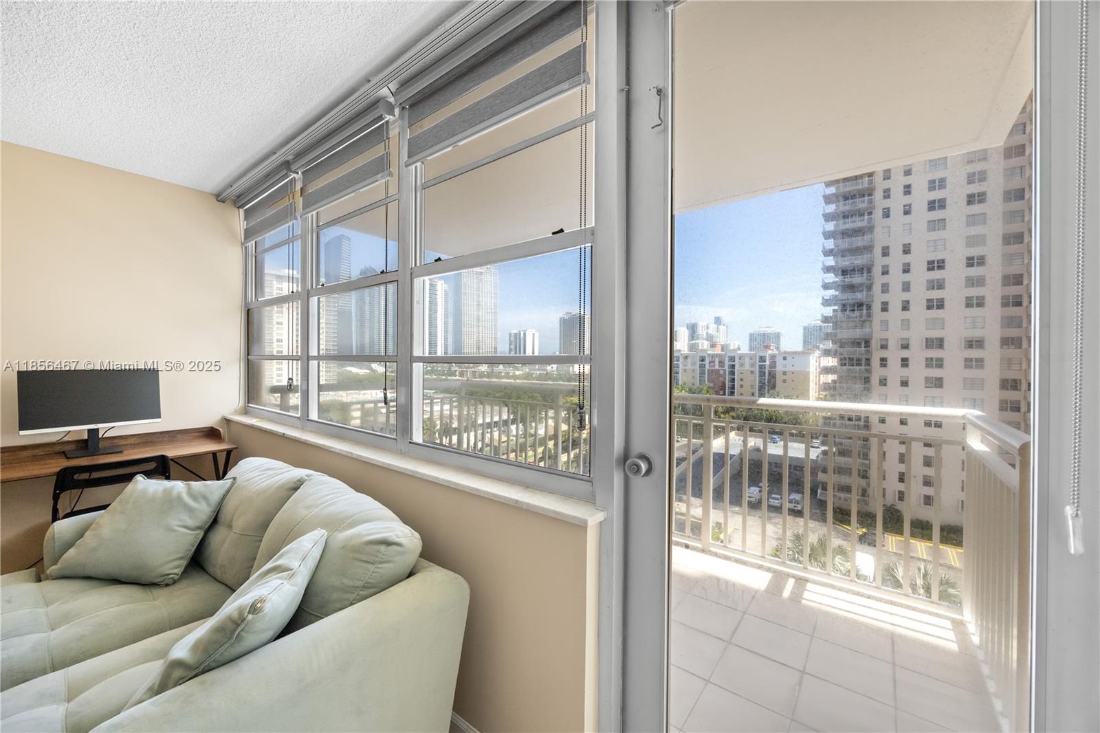 A living area features a light-colored sofa, a desk with a monitor, and a balcony — 251 174th St # 812, Sunny Isles Beach FL 33160, SUNNY ISLES BEACH, FL