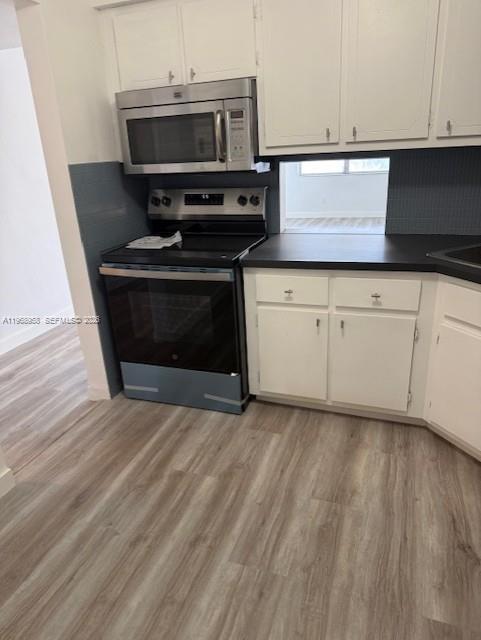 A kitchen features white cabinets, stainless steel appliances, a dark countertop, and light wood flooring — 1400 NE 191st St # 308, Miami FL 33179, MIAMI, FL