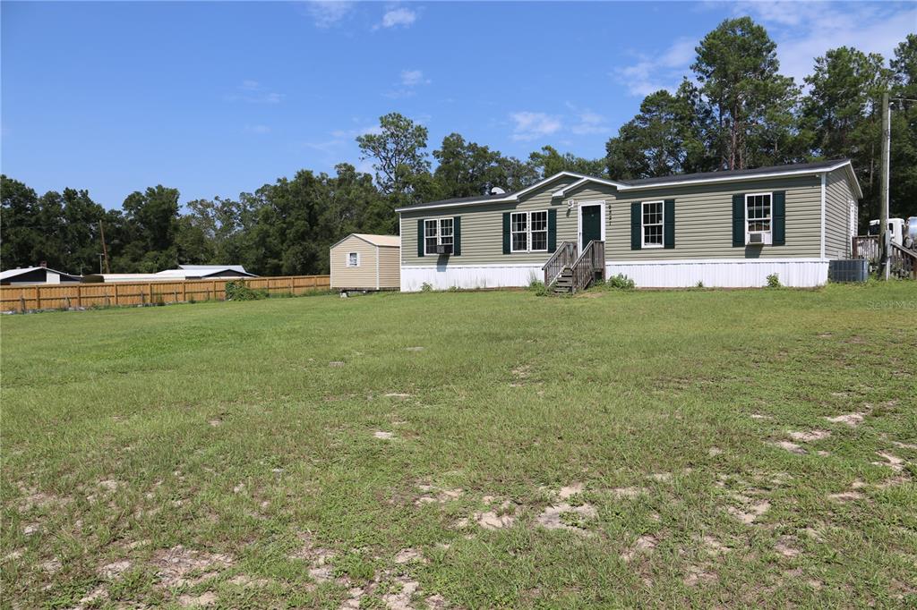 A single-story manufactured home with green siding sits on a large, grassy lot — 9521 NE 66TH LANE, BRONSON, FL