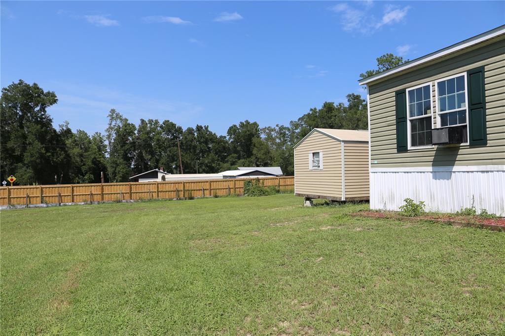 A grassy backyard features a small shed and a mobile home with green siding — 9521 NE 66TH LANE, BRONSON, FL