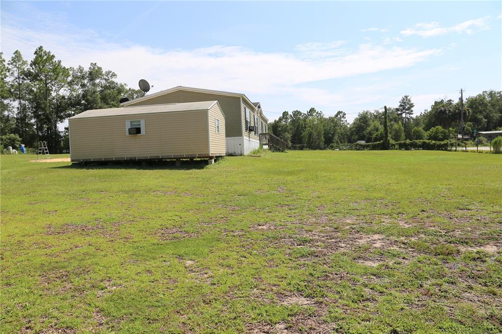 A tan mobile home sits on a large grassy lot with a matching storage shed — 9521 NE 66TH LANE, BRONSON, FL