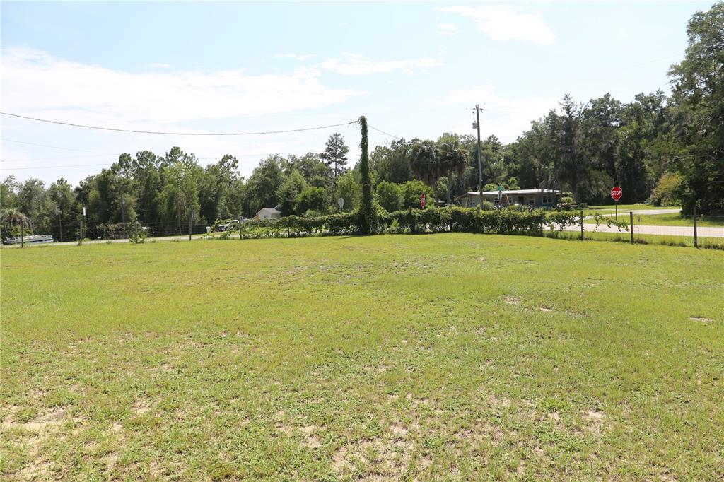 A large, grassy vacant lot is enclosed by a wire fence with trees in the background — 9521 NE 66TH LANE, BRONSON, FL