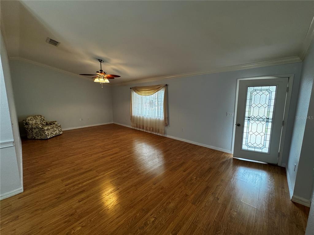 A spacious living room features light-colored walls, wood flooring, a ceiling fan, and a glass-paneled door — 17522 SE 95TH CIRCLE, SUMMERFIELD, FL