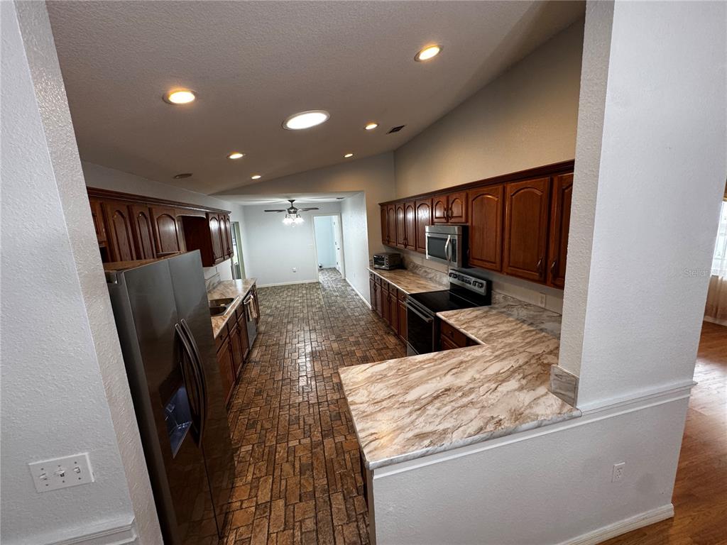 A kitchen features wood cabinets, marble-patterned laminate countertops, stainless steel appliances, and stone-look flooring — 17522 SE 95TH CIRCLE, SUMMERFIELD, FL