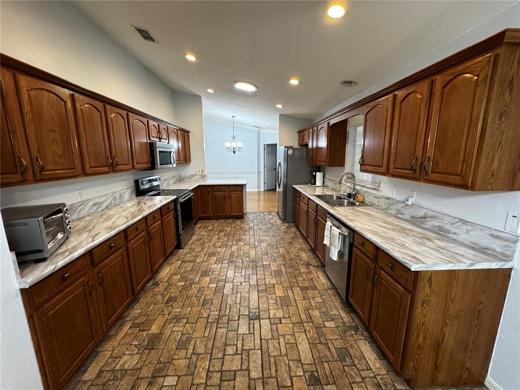 A galley kitchen features wood cabinets, marble-patterned laminate countertops, and a stone-look tile floor — 17522 SE 95TH CIRCLE, SUMMERFIELD, FL