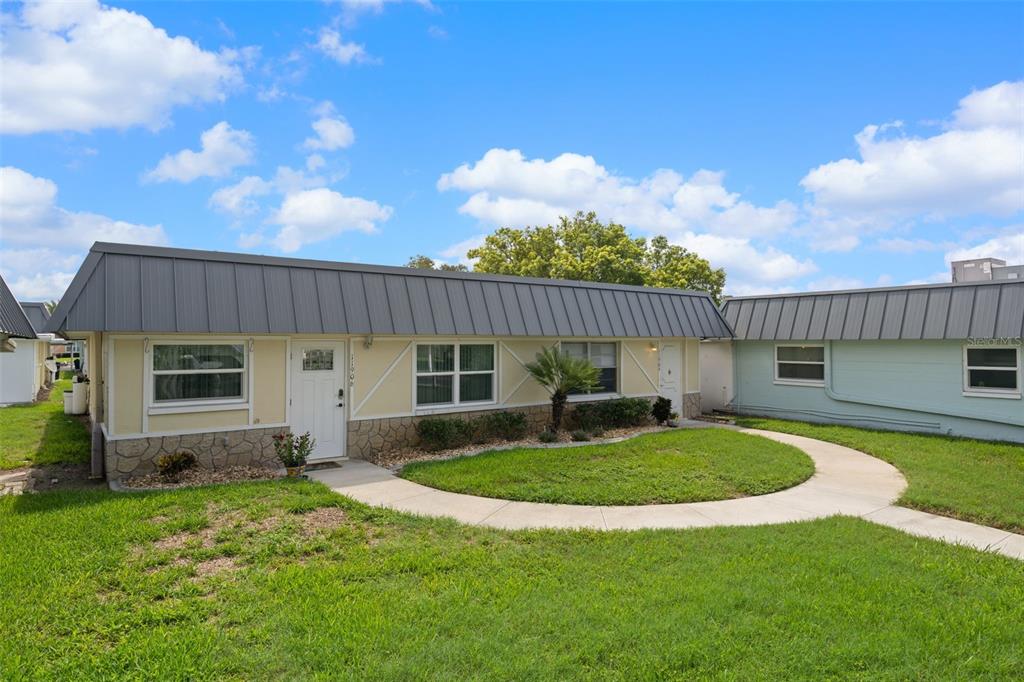 A single-story house with a metal roof, light-colored siding, and a stone facade base — 11904 BAYONET LANE, NEW PORT RICHEY, FL