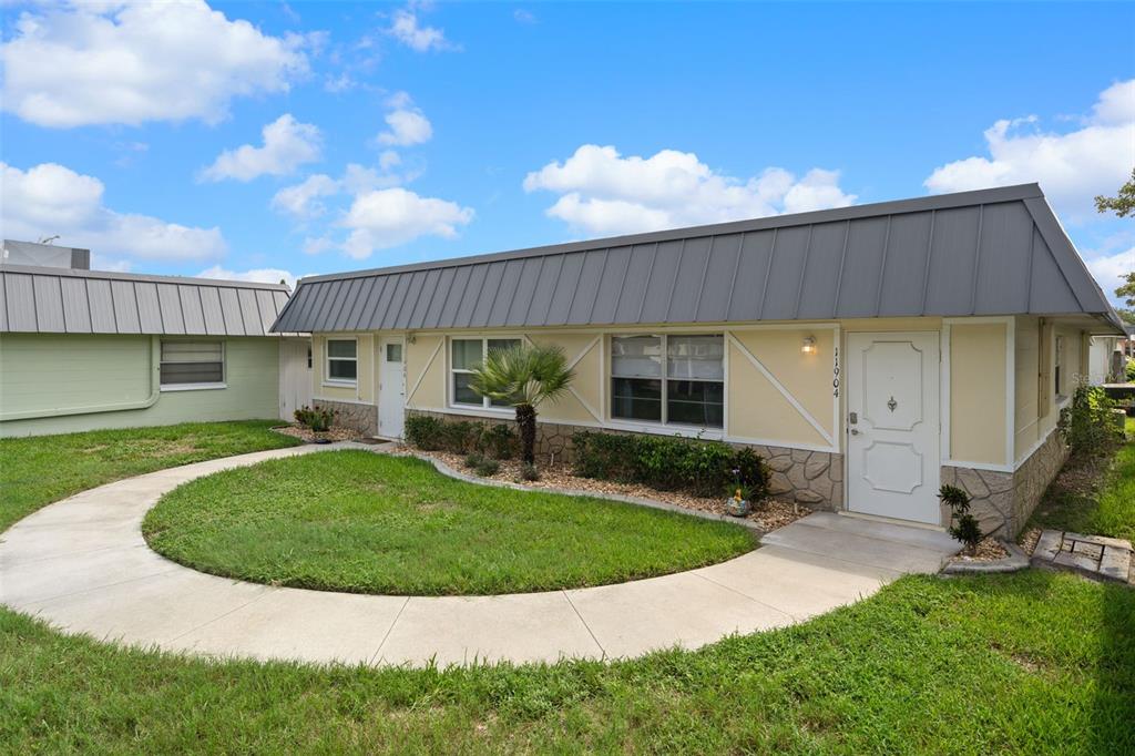 A single-story house with a metal roof, light yellow siding, and a stone-textured base — 11904 BAYONET LANE, NEW PORT RICHEY, FL