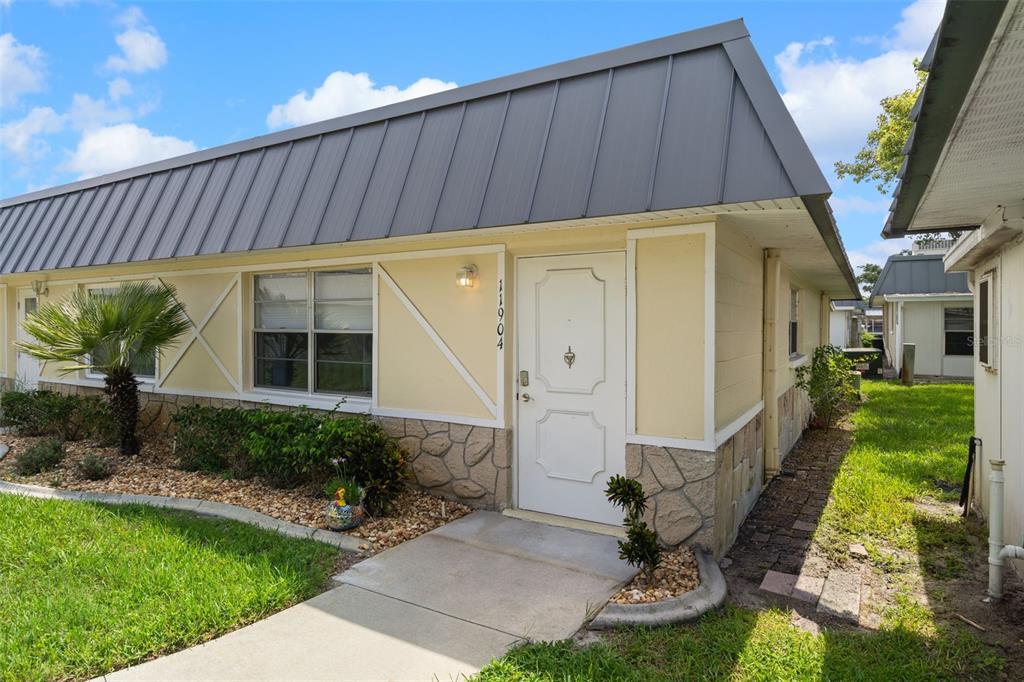 A single-story residential building with a metal roof, yellow siding, and a stone veneer base — 11904 BAYONET LANE, NEW PORT RICHEY, FL