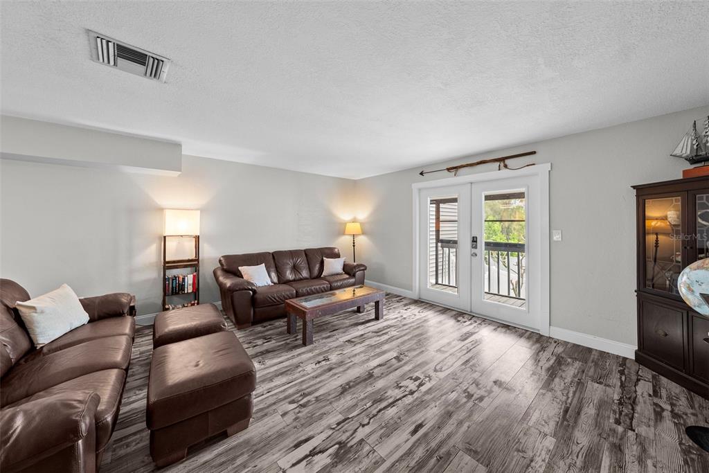 A living room features brown leather furniture, wood-look flooring, and glass doors leading outside — 619 2ND STREET UNIT 2, INDIAN ROCKS BEACH, FL