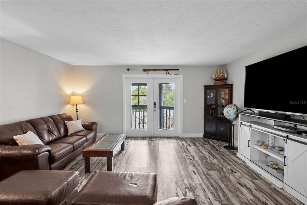 A living room features a brown leather sofa, wood-look flooring, and a large television console — 619 2ND STREET UNIT 2, INDIAN ROCKS BEACH, FL