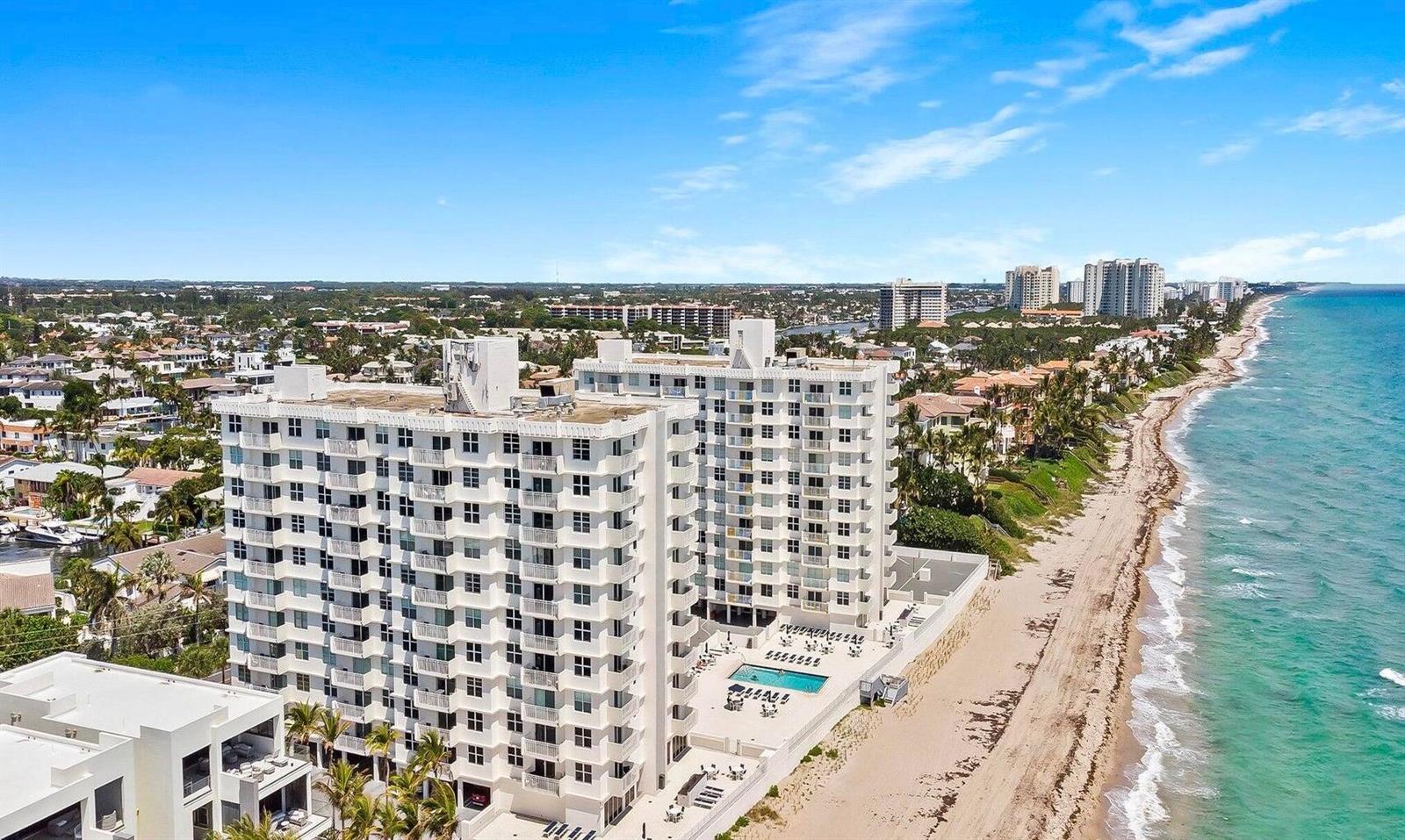 An aerial view shows a white multi-story apartment building situated directly on a sandy beach — 4511 S Ocean Boulevard # 807, Highland Beach FL 33487, HIGHLAND BEACH, FL