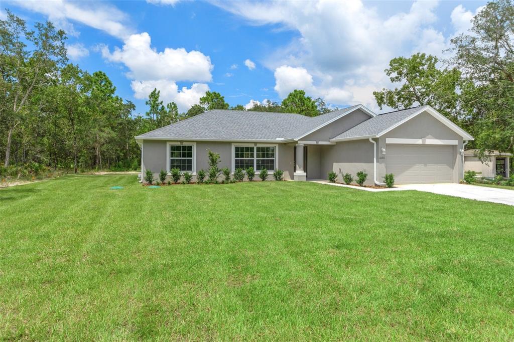 A single-story gray house with a two-car garage sits on a large grassy lot — 16375 KAKAWI ROAD, BROOKSVILLE, FL