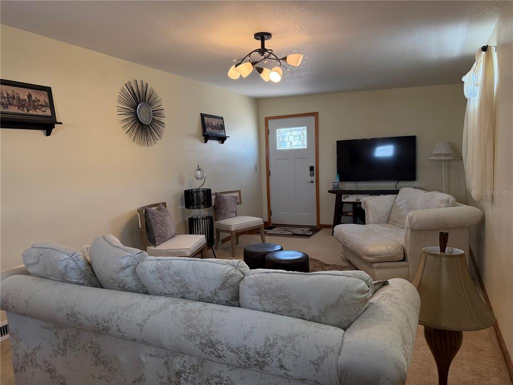 A living room features a light-colored sofa, two accent chairs, a television, and a door — 538 CENTER CREST BOULEVARD, DAVENPORT, FL