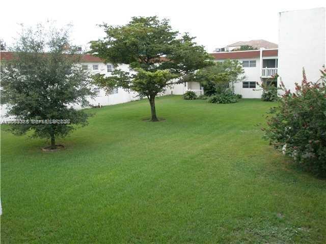 A grassy courtyard sits between two-story white apartment buildings with red roofs and trees — 4165 SW 67th Ave # 206B, Davie FL 33314, DAVIE, FL